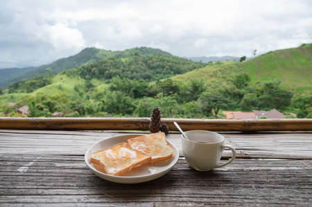 Breakfast with toast with hot chocolate in cup on wooden counter among the mountain view in the morningの写真素材