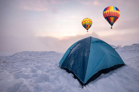Colorful hot air balloons flying on blue tent camping on snowy hillの写真素材