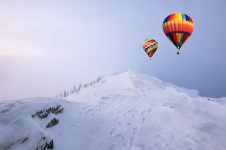 Colorful hot air balloons flying on snow hill in blizzardの写真素材