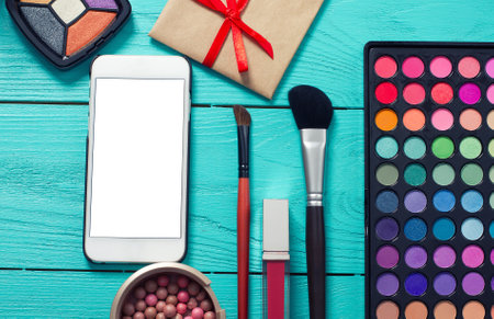 Frame of cosmetics and blank mobile screen on blue wooden background. Top view and copy spaceの写真素材