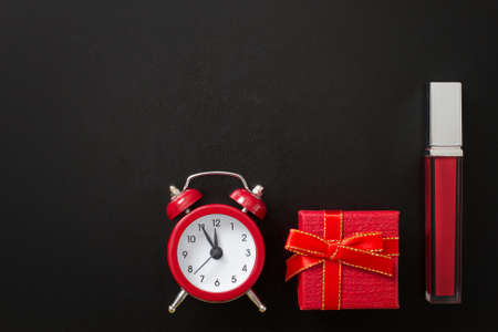 Lipstick cosmetic product with gift box and alarm clock isolated on black background. Sale time. Copy space. Top viewの写真素材