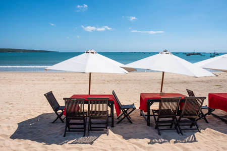 Red wooden dining table with white umbrella on the beach at Baliの写真素材
