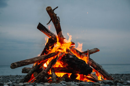 A bonfire on the beach. A bonfire on a stone beach. Fire on the beach - selective focus, copy space. Lonely fire on the seashore.の写真素材
