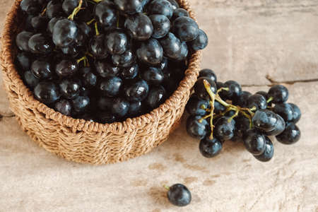 Bunch of black grapes in a round wicker basket on a old wooden table. Top view. Copy, empty space for text.の写真素材