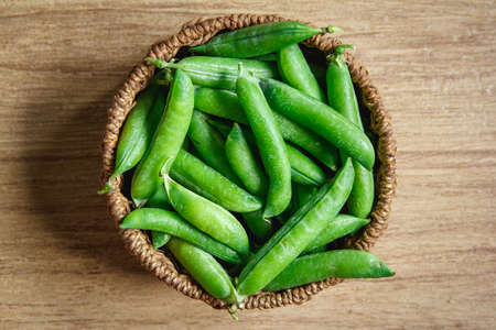 The crop of peas lies in a round wicker basket on a wooden background. Top view. Copy, empty space...