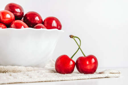 Fresh juicy red cherries in a white plate on the white wooden background. Copy, empty space for text.の写真素材