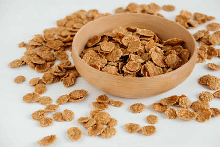 Crispy healthy dry cereal flakes in a wooden bowl on white background.