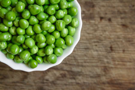 Fresh green peas in a white plate on wooden background, top view. Rustic table background.の写真素材
