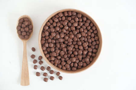 Chocolate corn balls in a wooden bowl and spoon scattered on a white background. Top view. Copy,...
