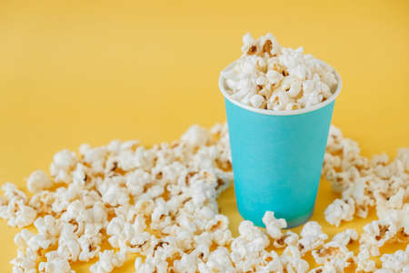 Popcorn in a blue paper cup on a yellow background. Minimalist concept. Copy, empty space for text.の写真素材