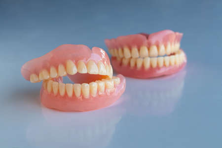 Close-up, the dentures of the two elderly were placed on a shiny table, white background to show...