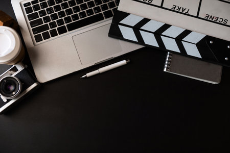 office stuff with Movie clapper, laptop, smartphone, tablet, coffee cup, pen, notepad and documents on the black table top view shot.の写真素材