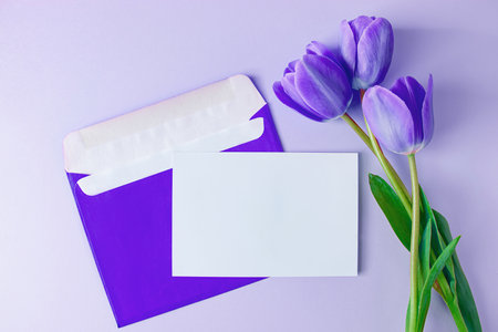 Envelope with invitation to holiday and bouquet of tulips on purple background. Trendy color of the...