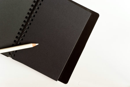 Black paper spiral notebook and white pencilの写真素材