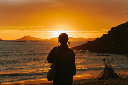 A traveler in front of a colorful sunset in the beach wearing a face mask, wellness concept, life and freedomの写真素材