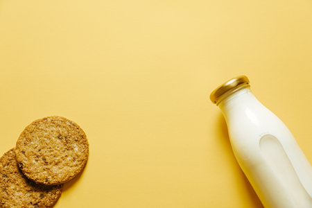 Two cookies and a bottle of milk over a yellow wallpaperの写真素材