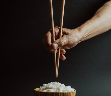 Minimalistic old hands grabbing japanese chopsticks over a bowl of rice concept shot on cinematic tones over a black backgroundの写真素材
