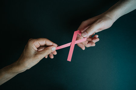 One old hand giving a pink ribbon to a young handの写真素材