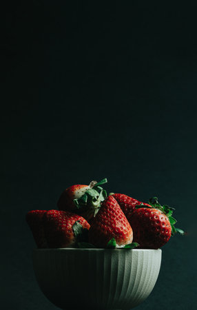 A minimal shot of a bunch of strawberries in a bowl over a dark background with copy spaceの写真素材