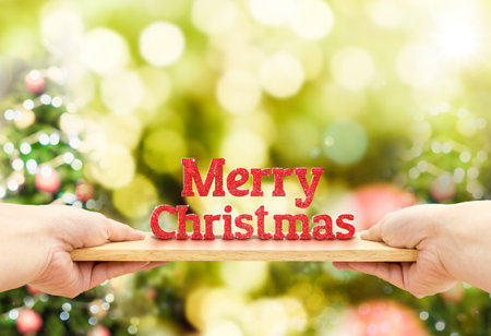 Hand holding wood plate with merry christmas red glitter number at blur christmas tree bokeh light background,Holiday conceptの写真素材