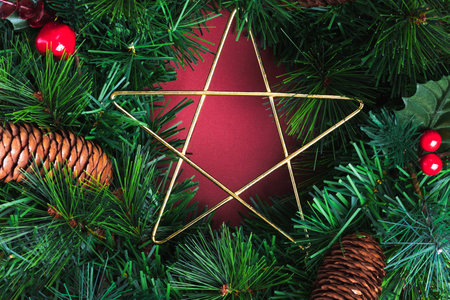 Close up star on green pine christmas wreath and pine cone ,cherry decoration item on red wall background.Celebration holiday festive greeing cardの写真素材