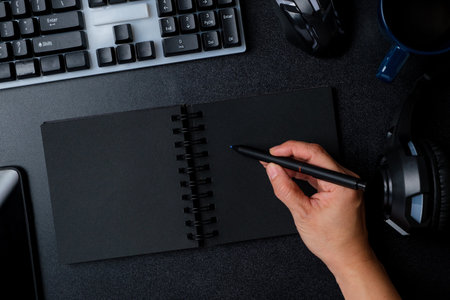 top view hand writing on notebook working on desk with keyboard headphone on black table backgroundの写真素材
