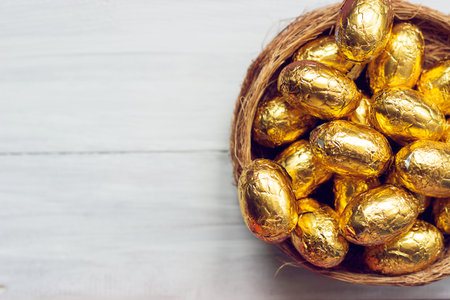 Golden easter eggs  - chocolate eggs in nest, on white wooden backgroundの写真素材