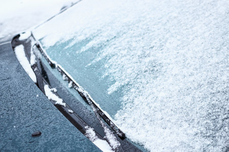 Close up of car windshield and wipers covered with ice and snow on a winter day