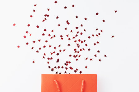Christmas shopping and birthday congratulation concept. Red shopping bag with festive glitter confetti on white backgroundの写真素材