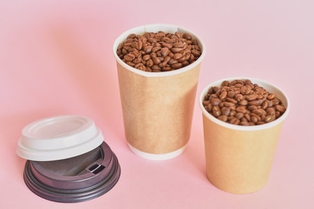 Two paper coffee cups with coffee beans on a pink backgroundの写真素材