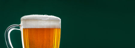 Mug with traditional Irish pale ale on dark green background. Bubbles in glass of beer. Banner format, place for textの写真素材