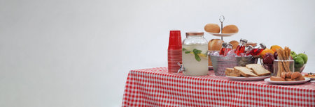 Picnic table and red checkered tablecloth with food and drink for outdoor party. Isolated white background. Wooden party table with foods and BBQ grills stove for summer picnics activities. Isolate.の写真素材