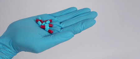 Taking or holding medication pills in hand. Capsule pill on white background isolated. Nitrile disposable gloves and medicines. Drugs healthcare treatment and supplement relieve symptomsの写真素材