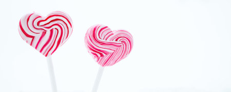 Two pink heart-shaped lollipop. Caramel candy on a stick on white background. Sweet gift for valentines day. Banner formatの写真素材