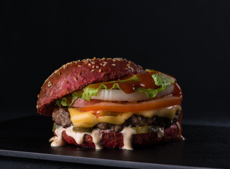 rumpled juicy cheeseburger on a flat plate on a black background, close - upの写真素材