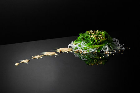 seaweed and onion with sesame seeds on a black background with reflection. a bundle of seaweed with onions on a dark surface with reflectionの写真素材