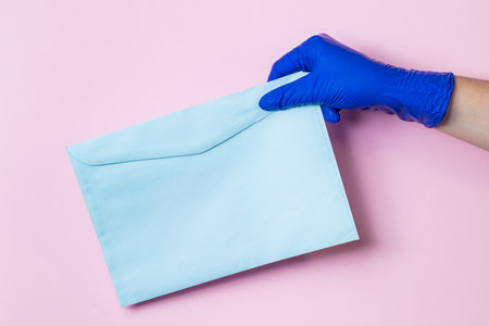 A man in medical latex gloves delivers an envelope on a pink background. The concept of safe delivery of goods during the coronavirus pandemic.の写真素材