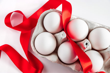White easter eggs in eco-friendly cardboard box with red festive silk ribbon on white background.の写真素材