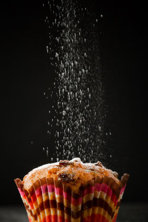 Tasty muffin in icing sugar on a black background. The process of making homemade cake. Vertical photo.の写真素材