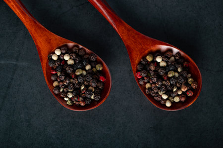 Wooden spoon with mix of pepper on a black background. Dried aromatic spice.の写真素材