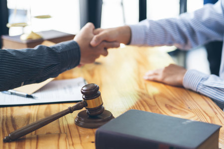 Businessmen shaking hands above the wooden desk in a modern office, close up. Unknown business people at meeting. Teamwork, partnership and handshake concept.の写真素材
