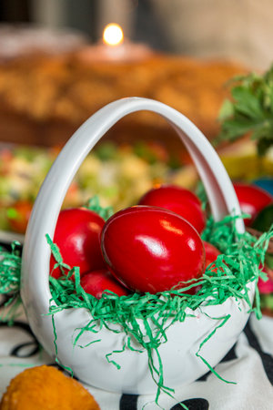 Easter table setting with colored red eggs, bread, green branches decorated, over white plank wooden...