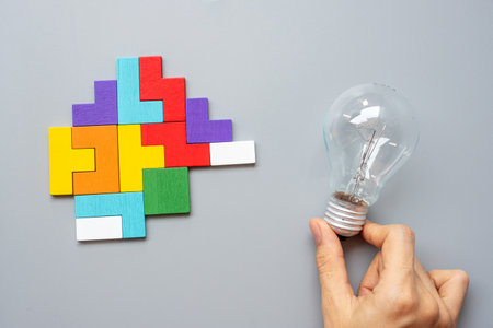 Hand holding lightbulb with colorful wood puzzle piece on gray background. New Idea, Creative, Innovation, Imagination, inspiration, Solution, Strategy and Logic conceptの写真素材