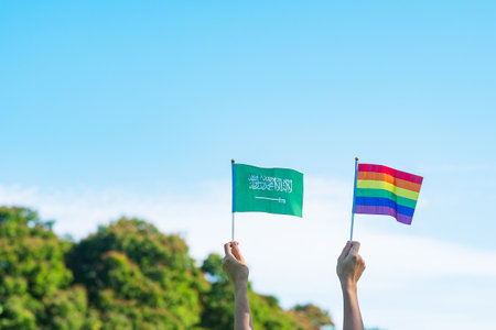 hands showing LGBTQ Rainbow and Saudi Arabia flag on nature background. Support Lesbian, Gay, Bisexual, Transgender and Queer community and Pride month conceptの写真素材