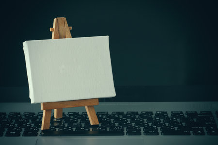 blank canvas and wooden easel on laptop computer as conceptの写真素材