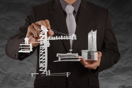 businessman hand shows house model with crumpled paper background as conceptの写真素材
