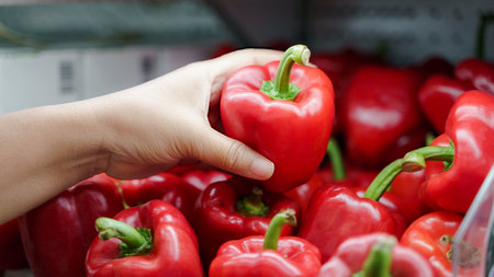 Close up woman hand holding fresh red bell pepper on the shelf at supermarket.の写真素材