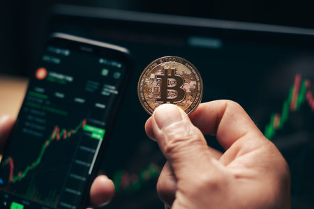 Businessman holding golden bitcoin on computer trading chart screen background. stock,...
