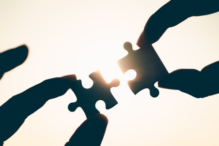 Silhouette of closeup woman and man hand connecting a piece of jigsaw puzzle over sunlight effect....