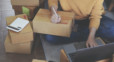 Startup Entrepreneurship Small Business SME Freelance Young lady working at home with boxes on the floor and laptop online Marketing Packaging SME Shipping Ecommerce Conceptsの写真素材